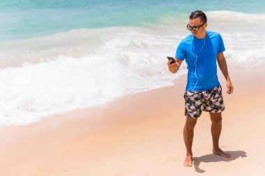 Mutlu genç adam beyaz kumlu plaj üzerinde müzik keyfi