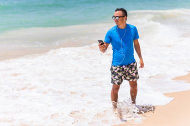 Mutlu genç adam beyaz kumlu plaj üzerinde müzik keyfi