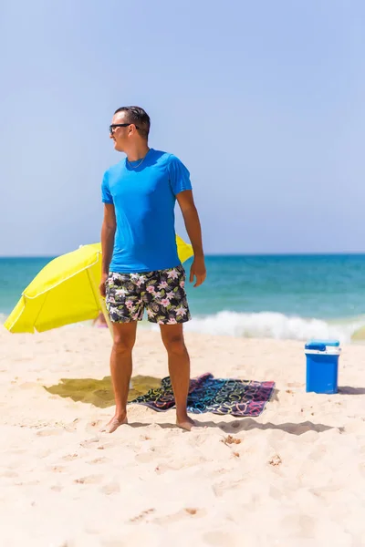 Ένας άνθρωπος που μεταφέρουν μια πράσινη ομπρέλα και στέκεται στην παραλία κοιτάζοντας στην παραλία — Φωτογραφία Αρχείου
