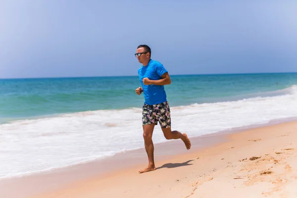Мужчина бежит по солнечному пляжу возле океана — стоковое фото