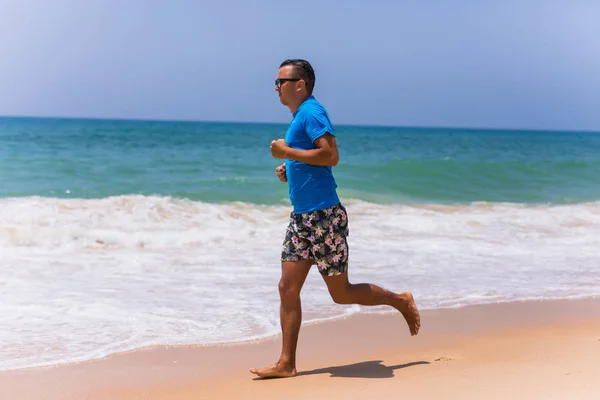 Человек бегущий по тропическому пляжу делает спорт — стоковое фото