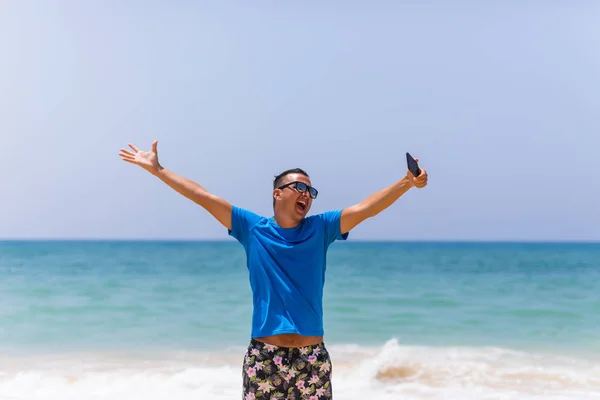 Молодой человек держит мобильный телефон сфотографировать летний пляж панорамный вид на море — стоковое фото
