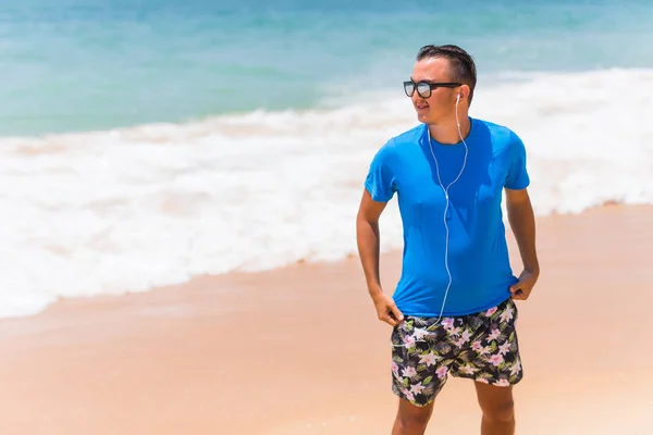 Enjoying music sports lifestyle happy young man in headphones walking on the sea shore — Stock Photo, Image