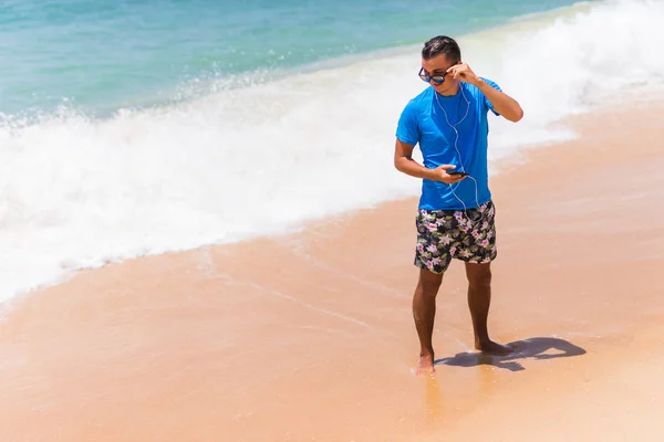 Счастливый молодой человек наслаждается музыкой на белом песчаном пляже — стоковое фото