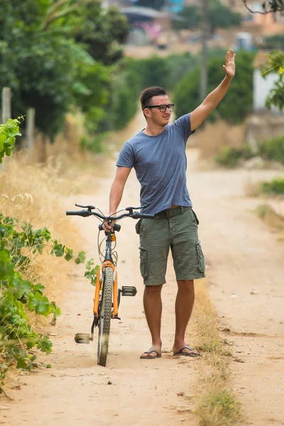 Pohledný muž v brýlích slunce se usmívá při cyklistice v parku — Stock fotografie