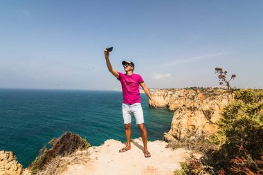 Genç adam almak selfie ve Atlantik Okyanusu dalgaları yakınındaki kaya