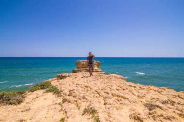 Yürüyen adam ve plajda kayalar ile Atlantik Okyanusu ve kayalıklarla, algarve Portekiz manzarasının keyfini çıkarın. Yaz meslek kavramı