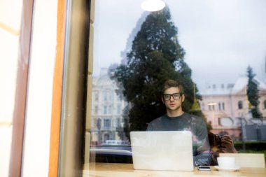 Genç adam bilgisayar kullanarak kafede kahve içme