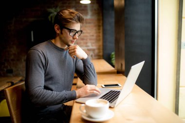 Kafe Durin'in çalışmalarında otururken bir dizüstü bilgisayar üzerinde çalışan genç başarılı serbest