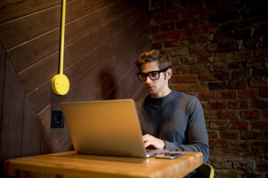 Bir fincan kahve ile kafede dizüstü bilgisayar kullanan genç adam