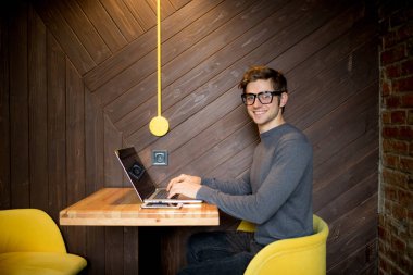 Bir fincan kahve ile kafede dizüstü bilgisayar kullanan genç adam