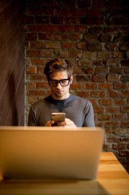 Çekici bir adam cep telefonda konuşurken ve çalışma kahve dükkanı gülümseyen bir laptop kullanıyor