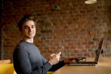 Kafede oturan ve laptop ve cep telefonu kullanarak genç adam