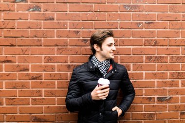 Genç bir adam elinde kahvesiyle bir tuğla duvar zemin karşı 