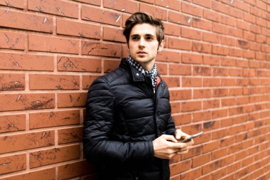 Cep telefonu tuğla duvara yaslanmış Ise tutarak Akıllı rahat kıyafet kız yakışıklı genç adam için manifatura