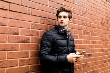 Cep telefonu tuğla duvara yaslanmış Ise tutarak Akıllı rahat kıyafet kız yakışıklı genç adam için manifatura