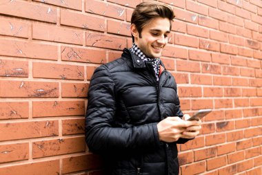 Hareket eden telefon tutarak ve duran tuğla duvara bakarak yakışıklı delikanlı