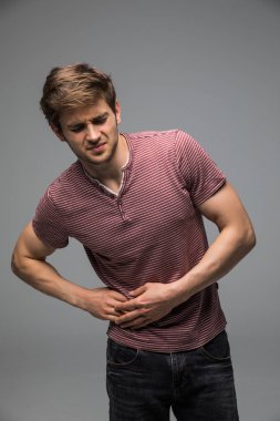 Mide sorunları ve gri arka plan üzerinde duran yakışıklı adam 