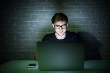 Internet'e bağlanma ve gece geç saatlerde bir dizüstü bilgisayar kullanarak gülümseyen genç adam