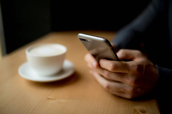 Man gebruikt zijn telefoon in de koffieshop met kopje koffie — Stockfoto