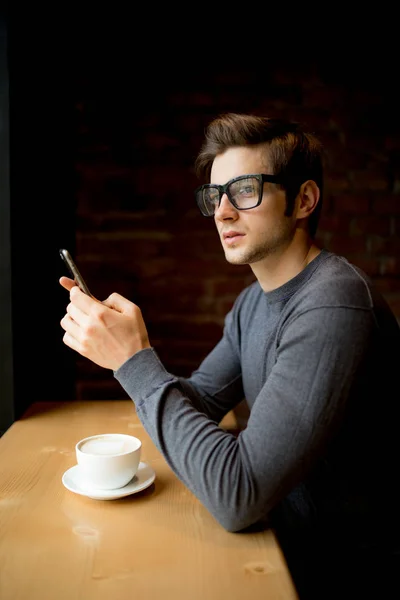 Inviting friend for coffee handsome young man holding smart phone and looking at it while sitting