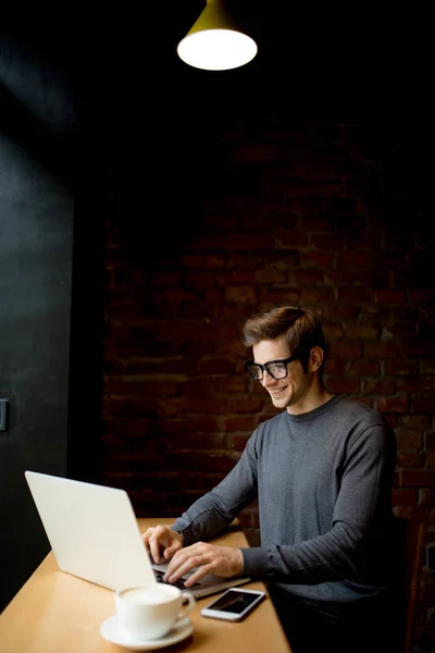 Retrato de un joven sonriente usando un portátil en la cafetería — Foto de Stock