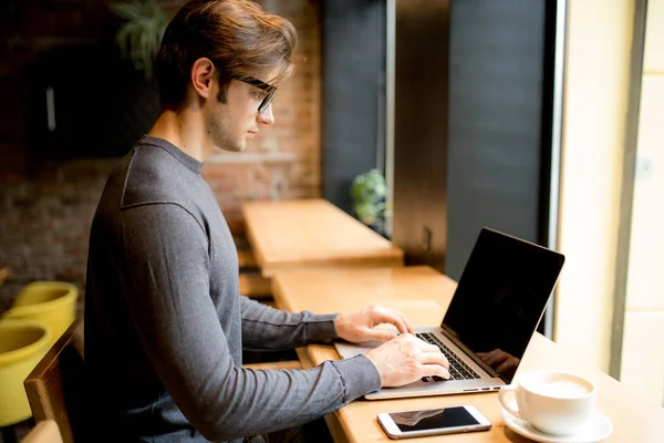 Vista lateral del hombre con el ordenador portátil sentado en la cafetería y el trabajo — Foto de Stock