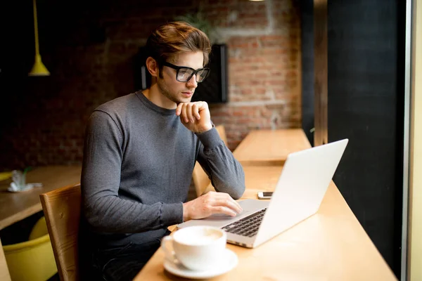 Joven empresario exitoso trabajando en un ordenador portátil mientras está sentado en la cafetería durin trabajo — Foto de Stock