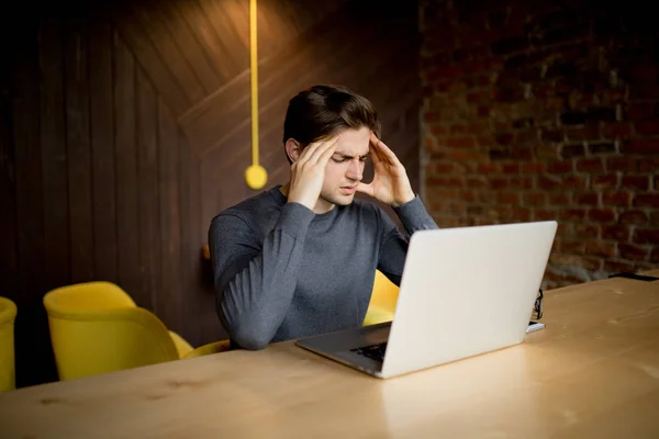 Knappe jonge man aan het werk op laptop met droevig gezicht of hoofdpijn werken bij laptop — Stockfoto