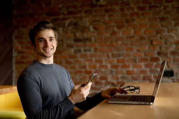 Kafede oturan ve laptop ve cep telefonu kullanarak genç adam — Stok fotoğraf
