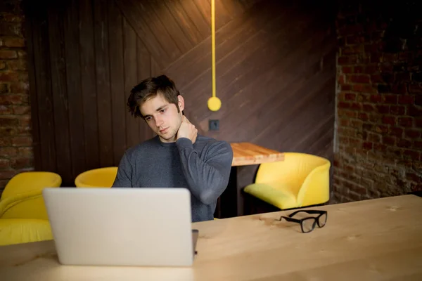 Bonito homem sofrendo de dor no pescoço no escritório no laptop — Fotografia de Stock