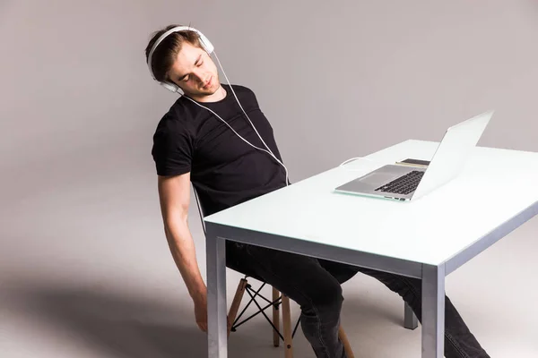Joven dormir mientras usa auriculares y trabajar en el ordenador portátil en la mesa de su oficina sobre fondo blanco. trabajo —  Fotos de Stock