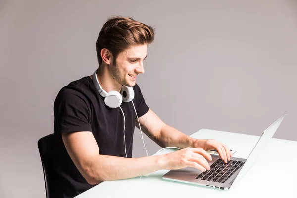 Imagem de um jovem na mesa do computador trabalhando em laptop com fones de ouvido em branco — Fotografia de Stock