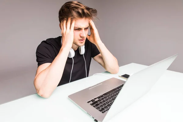 Pohledný mladý muž trpí bolesti hlavy při práci s notebookem na šedém pozadí — Stock fotografie