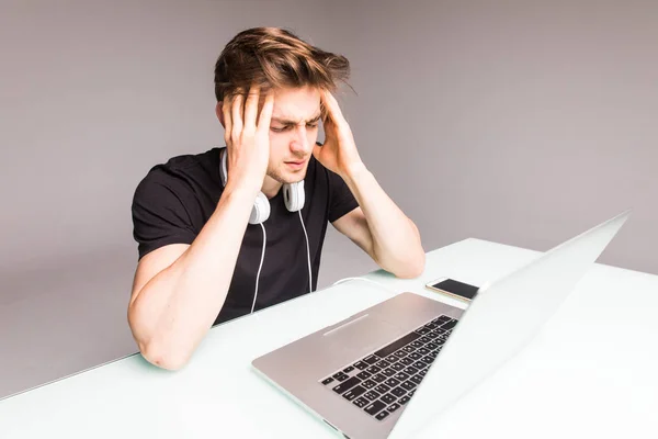 Schöner junger Mann, der unter Kopfschmerzen leidet, während er mit Laptop auf grauem Hintergrund arbeitet — Stockfoto