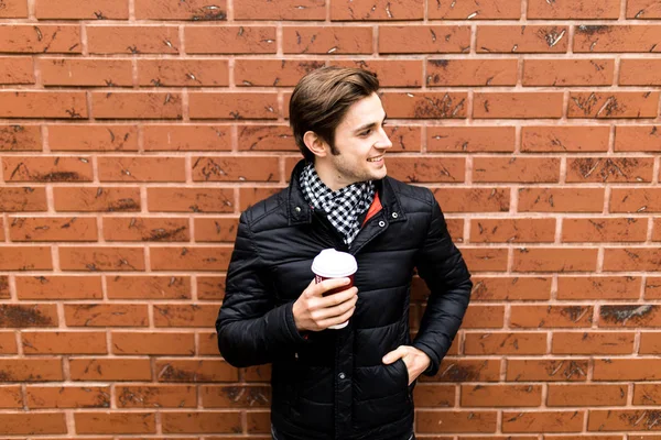Um jovem contra o pano de fundo de uma parede de tijolos com café na mão — Fotografia de Stock