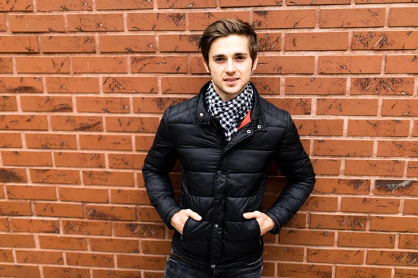 Gülümseyen ve tuğla duvara bakarak cebinde eliyle oturan serin moda adam