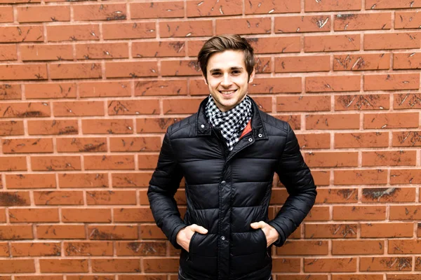 Gülümseyen ve tuğla duvara bakarak cebinde eliyle oturan serin moda adam