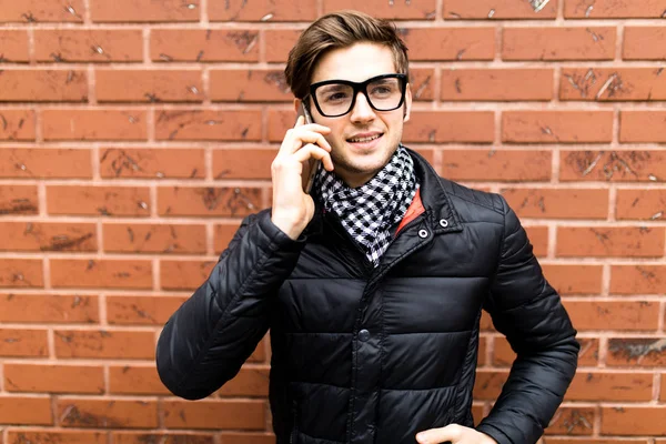 若いハンサムな男の携帯スマート電話がレンガの壁で笑顔を話す — ストック写真