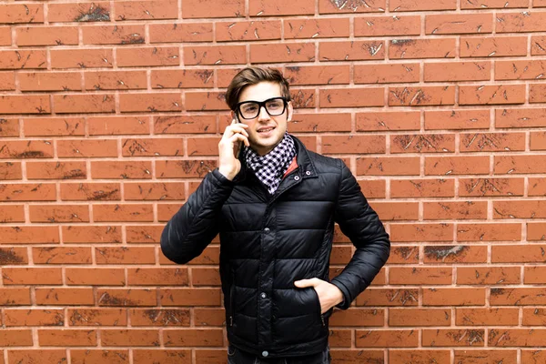 Yakışıklı delikanlı hücre akıllı telefon görüşmesi konuşmak gülümseme tuğla duvarın üzerinden