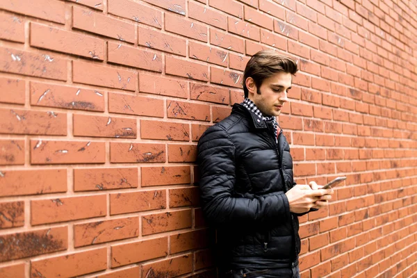 Hareket eden telefon tutarak ve duran tuğla duvara bakarak yakışıklı delikanlı