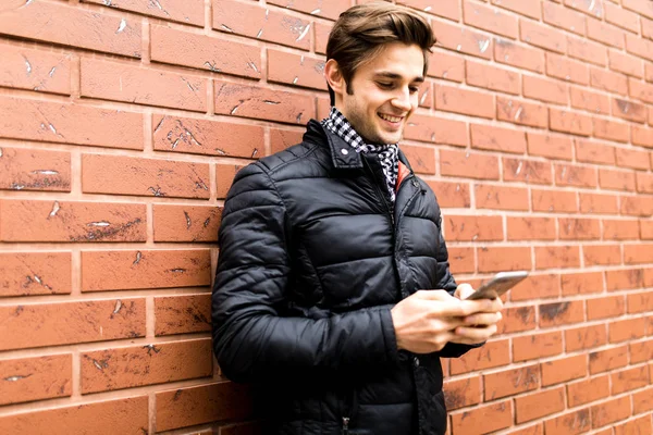 Hareket eden telefon tutarak ve duran tuğla duvara bakarak yakışıklı delikanlı