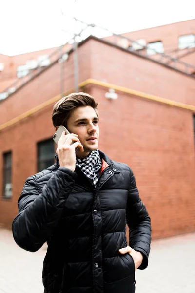 Jovem bonitão falando ao telefone na rua no prédio de tijolos — Fotografia de Stock