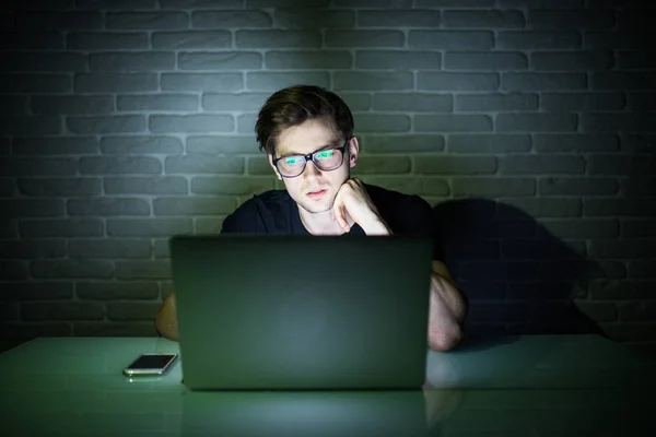 Młody człowiek uśmiechający się ręką na podbródek, podłączenie do Internetu i komputera przenośnego późno w nocy — Zdjęcie stockowe