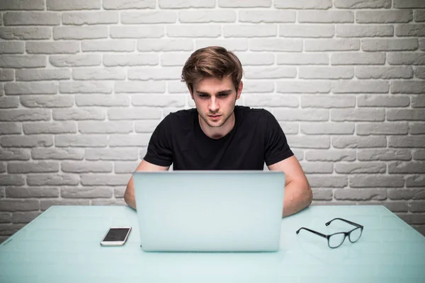 Casualmente vestido jovem designer ouvir música em fones de ouvido enquanto trabalhava em um laptop — Fotografia de Stock