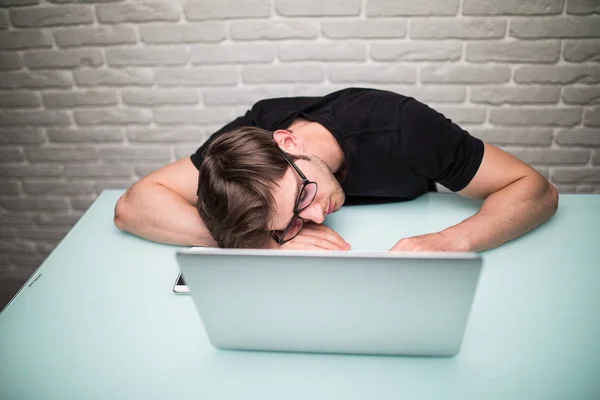 Junger gutaussehender Mann mit Computer im Büro denkt über Aufgabe bei der Programmierung nach, schlafend auf Arbeitstisch — Stockfoto