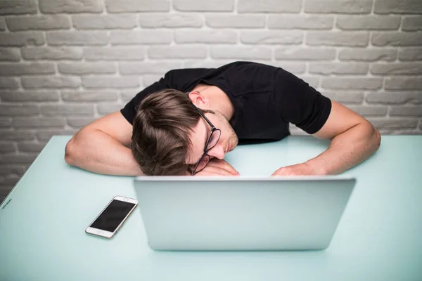 Junger gutaussehender Mann mit Computer im Büro denkt über Aufgabe bei der Programmierung nach, schlafend auf Arbeitstisch — Stockfoto