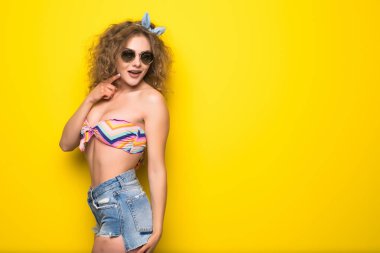 Genç güzel kıvırcık kadın güneş gözlüğü Sarı zemin üzerine mutlu gülümseme ile