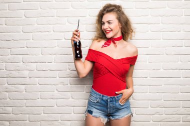 Şık genç kız duvara karşı bir şişe soda su tutuyor