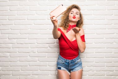 Bir tuğla duvar arka planda bir akıllı telefon kendi kendine portre yapma güzel genç kadın